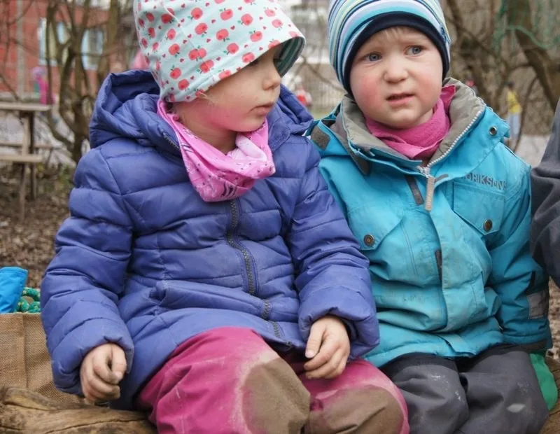 Zwei Kinder sitzen in Winterjacken draussen beieinander